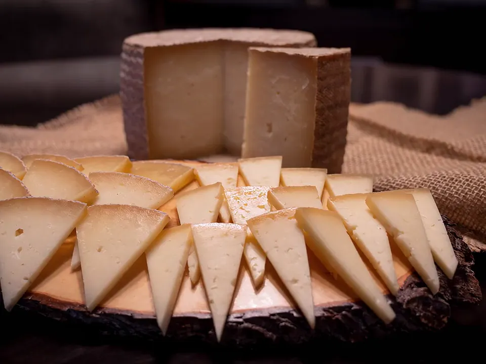 Queso de oveja curado cortado en cuñas sobre una tabla de madera